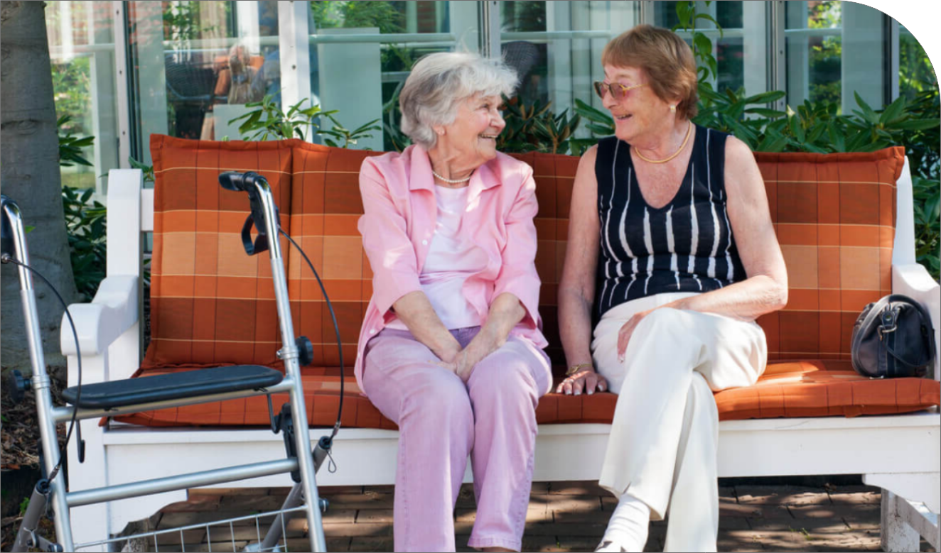 Two senior women sitting on a bench and laughing together in front of their retirement residence.