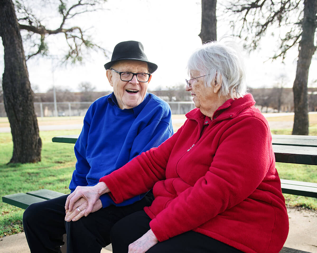 Okanagan seniors holding hands while sitting on park bench